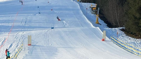 Menschen beobachten ein Skirennen auf einer verschneiten Piste, während sie auf einer Terrasse sitzen und die Sonne genießen.