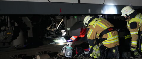 Feuerwehrleute arbeiten konzentriert unter einem Zug, während sie eine Rettungsaktion bei Nacht durchführen.